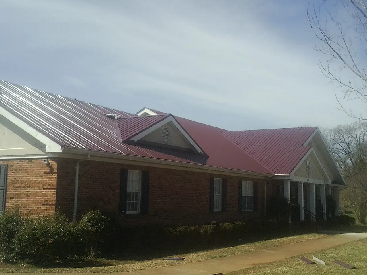 Red metal roof with gabled entries on a long brick building, from a Hail Damage Roof Repair job in Hookerton