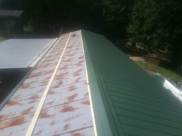 Old rusted panels beside newly installed green metal roofing — Wind Damage Roof Repair by Roofing Brothers in Hookerton