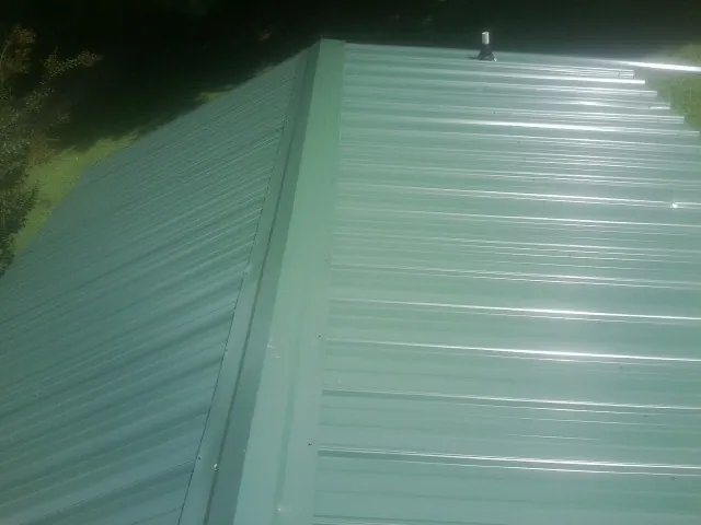New green metal panels meeting at the ridge of a roof — Flat Roof Repair work by our crew in Hookerton