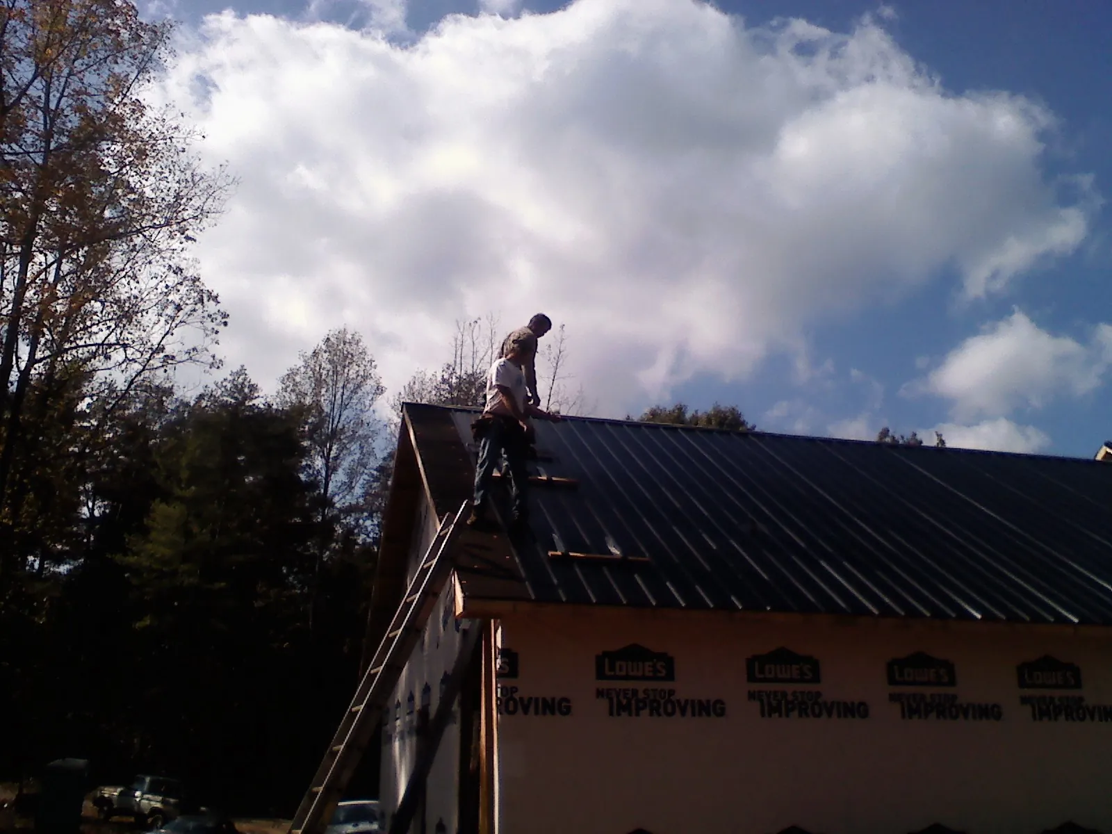Roofer fastening dark metal panels high against a cloudy sky, from a Roof Inspection job in Hookerton